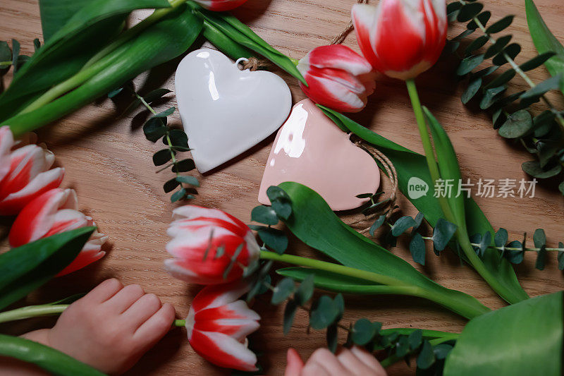 Bouquet of tulips on the table with hearts. Сhildren's hands hold flowers. Valentines, mothers, womens day, wedding or birthday flat lay concept. Top view.